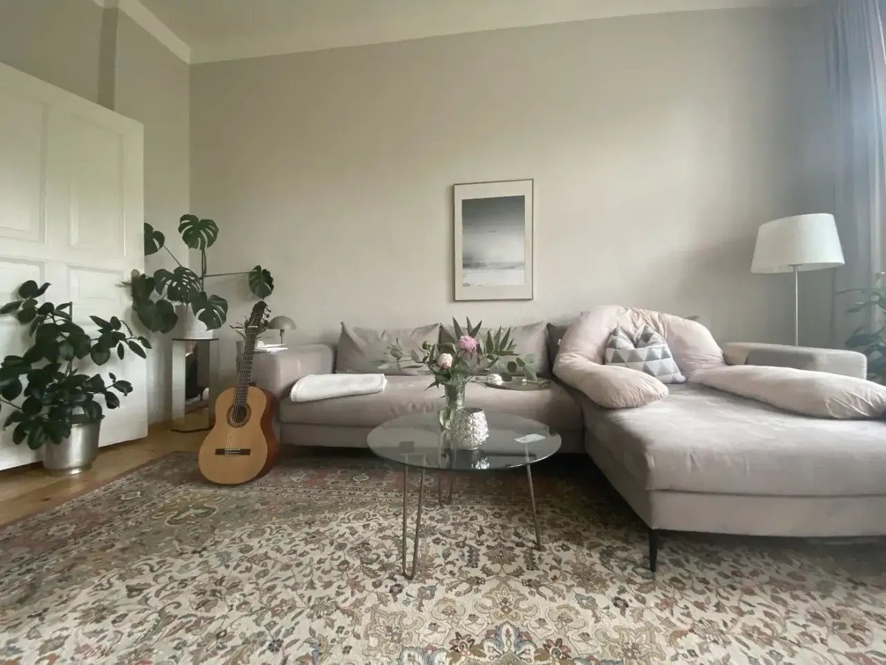 Gemütliches Wohnzimmer mit einem Ecksofa in greige Farbe, einer Gitarre und Pflanzen.