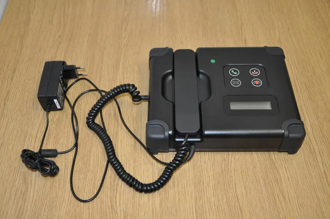 Czarny telefon z zasilaczem, część systemu dozoru elektronicznego. Długość kabla nie określa zasięgu.