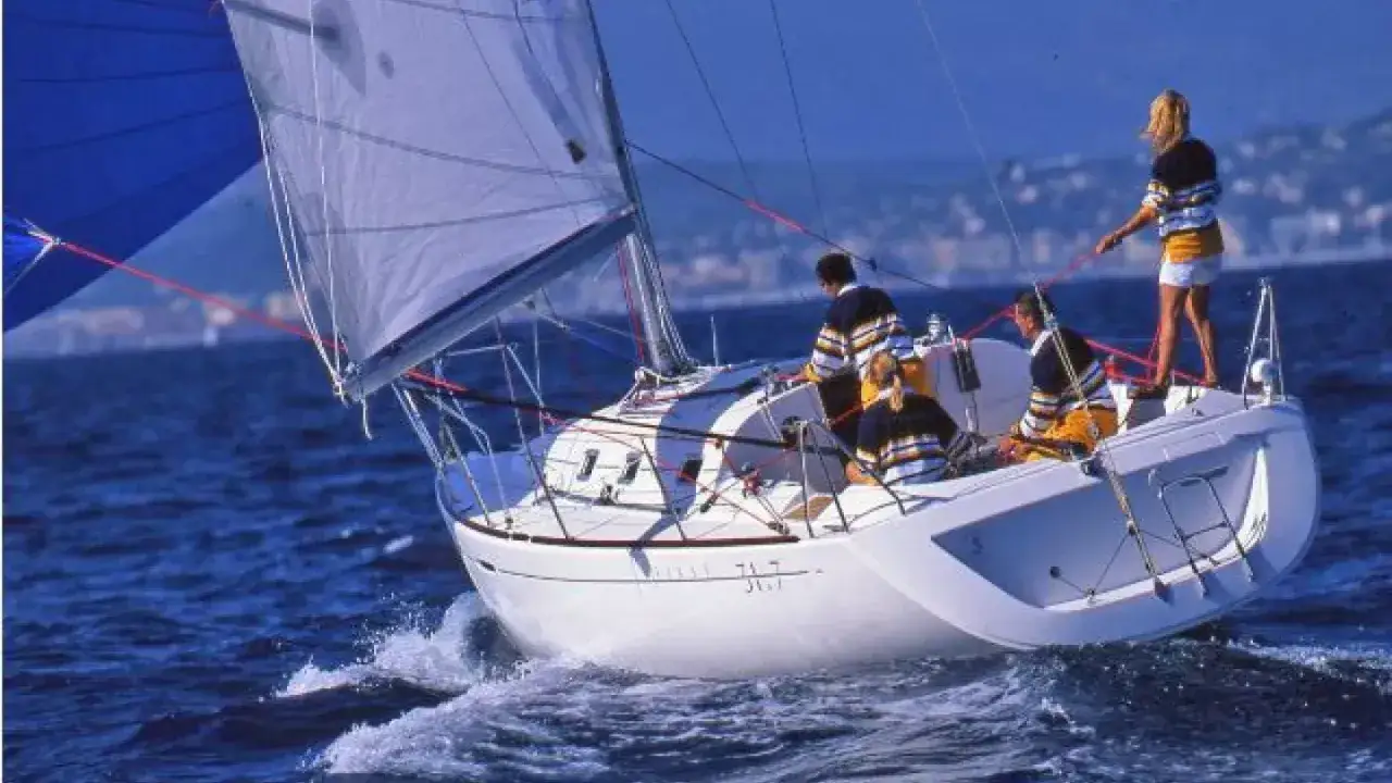Voile blanche et bleue sur un voilier blanc, le 31.7, naviguant sur une mer bleue avec quatre personnes à bord.