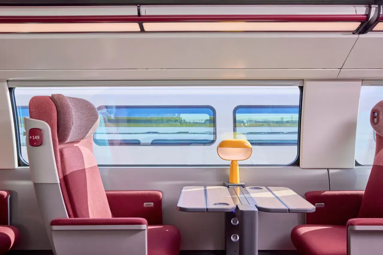 Interior of a modern bullet train, perfect for a Paris to Nice journey. Comfortable seats, a fold-out table, and a stylish lamp await.