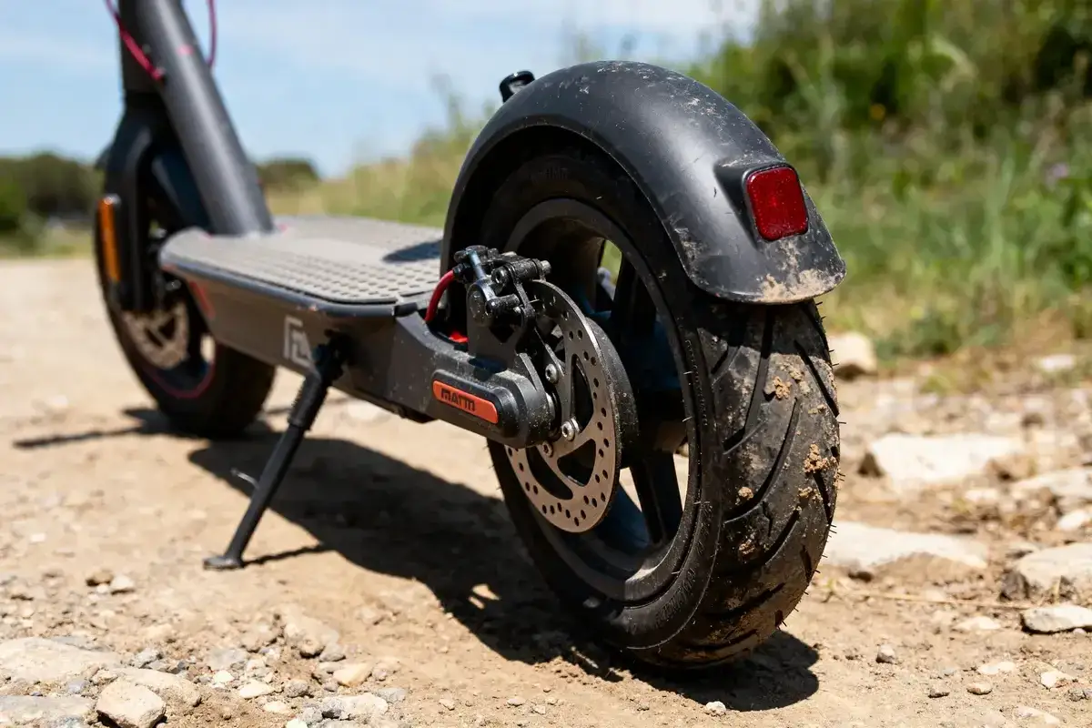 Roues de trottinette &eacute;lectrique sur terrain rocailleux. Le pneu arri&egrave;re est sale, sugg&eacute;rant qu'il est impossible de gonfler le pneu de la trottinette.
