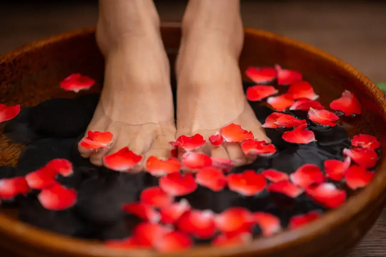 A relaxing foot detox bath with red rose petals floating in water with smooth black stones.