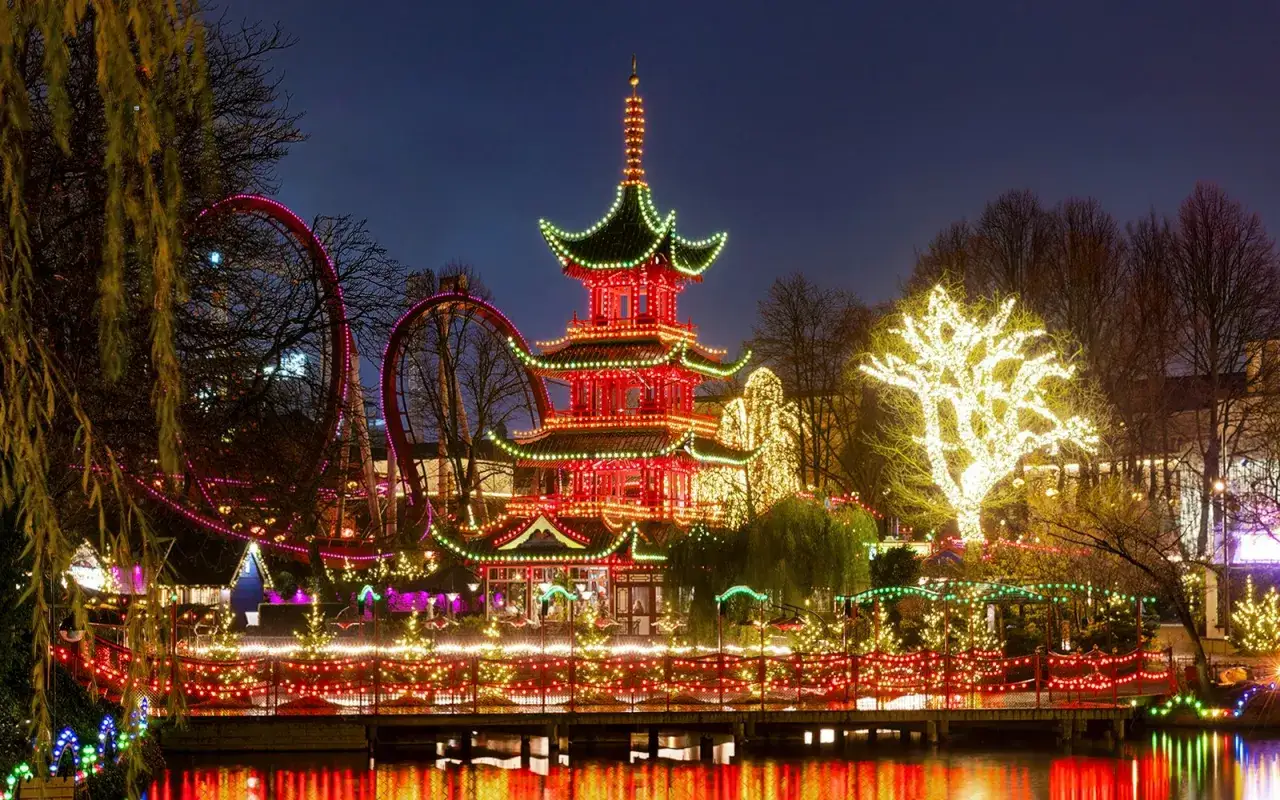 Magiczny park Tivoli Kopenhaga nocą. Czerwona pagoda i karuzela w blasku tysięcy światełek, odbijających się w wodzie.