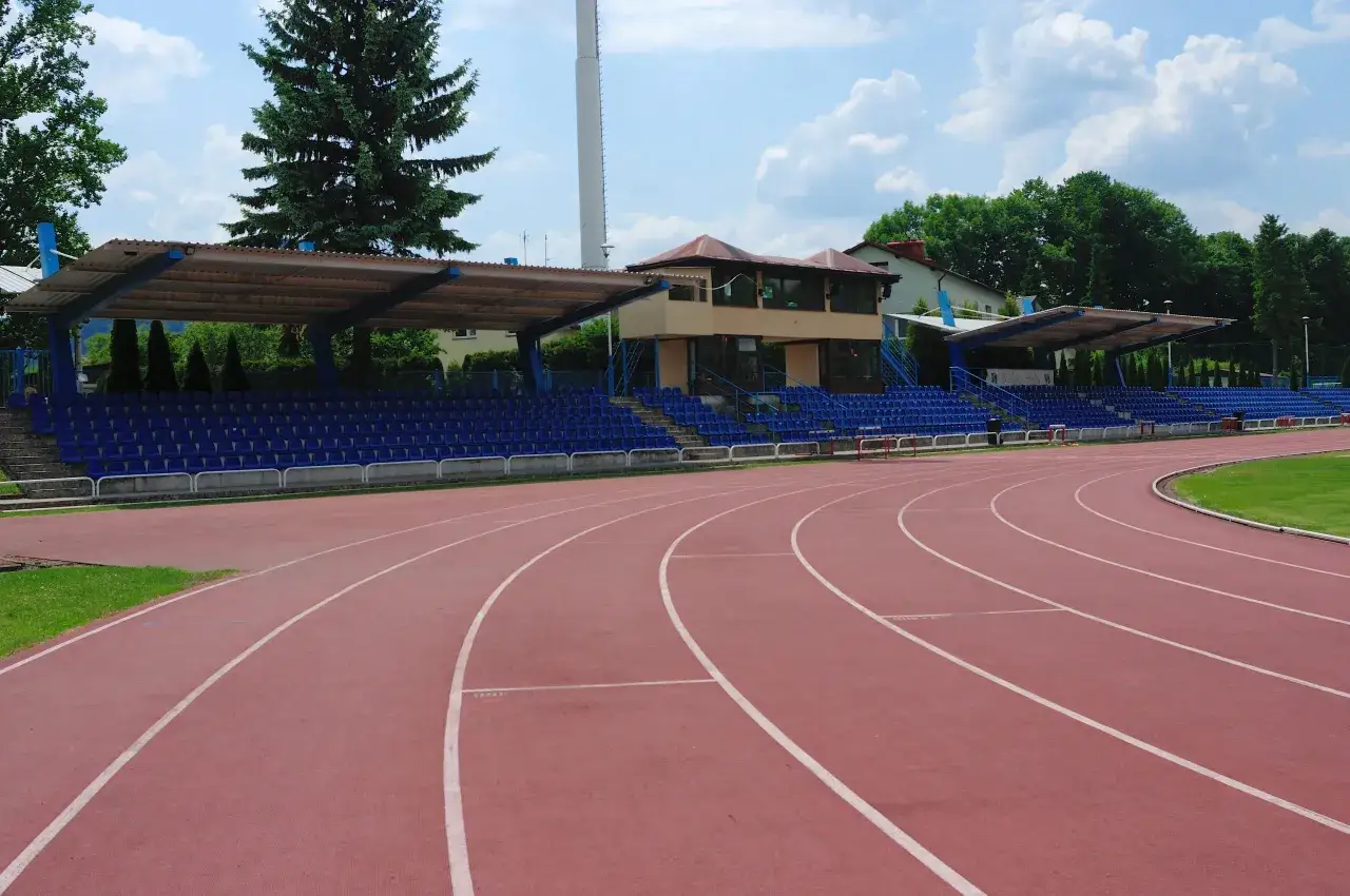 Pusta bieżnia stadionu, gotowa na bieg na 400 metr&oacute;w. Niebieskie trybuny czekają na kibic&oacute;w.