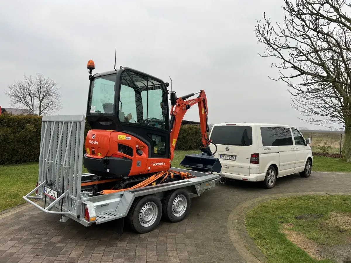 Pomarańczowa mini koparka Kubota na przyczepie, gotowa do transportu. Zastanawiasz się, ile kosztuje mini koparka?