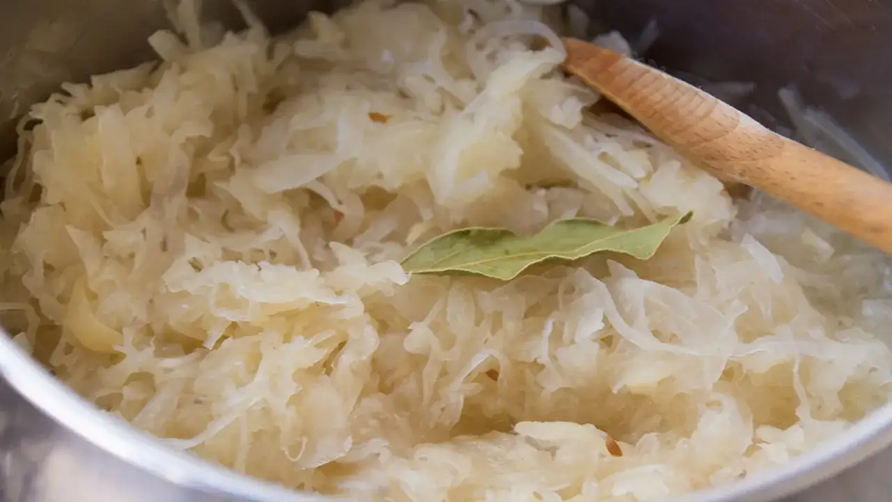 Frisch zubereitetes Sauerkraut mit einem Lorbeerblatt und einem Holzl&ouml;ffel. Perfekt als Beilage zu deftigen Speisen, vielleicht mit einem Glas Wein.