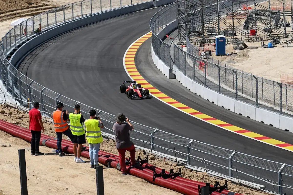 Un coche de Fórmula 1 rojo y blanco compite en una curva. Aficionados con chalecos reflectantes observan. ¡Noticias de Fórmula 1 en directo!