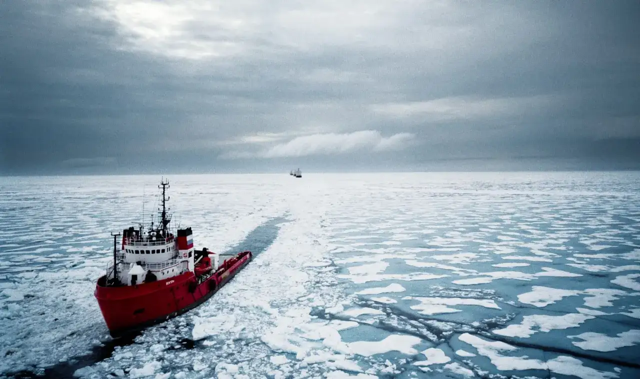 Una nave rompighiaccio rossa solca le acque del nord, aprendo un varco nel ghiaccio. Altre navi all'orizzonte.