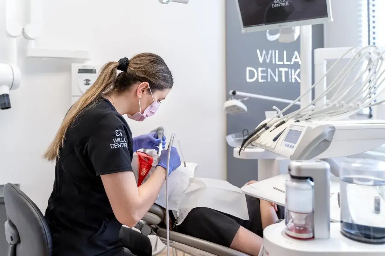 Dentystka w masce wykonuje higienizację zębów pacjentowi w gabinecie stomatologicznym.