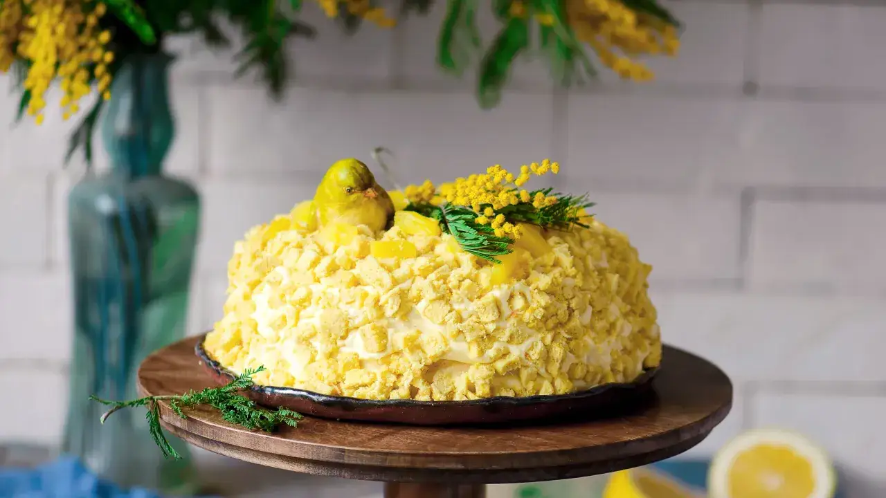 Torta mimosa decorata con un uccellino giallo e fiori di mimosa, pronta per festeggiare la primavera.