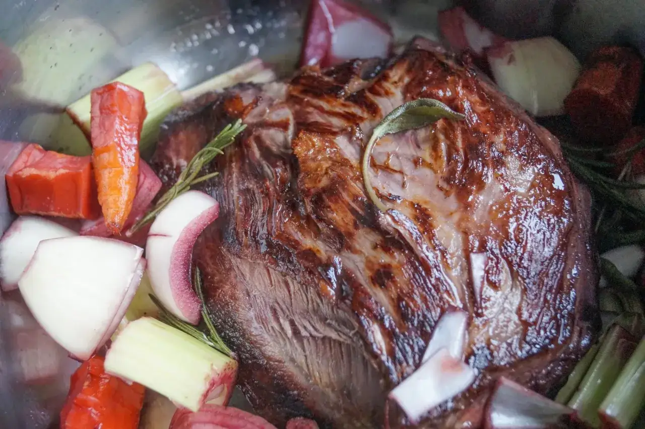 Ein Bratenst&uuml;ck mit Karotten, Zwiebeln und Kr&auml;utern in einem Topf. Perfekt, um Fleisch selber marinieren und langsam zu schmoren.
