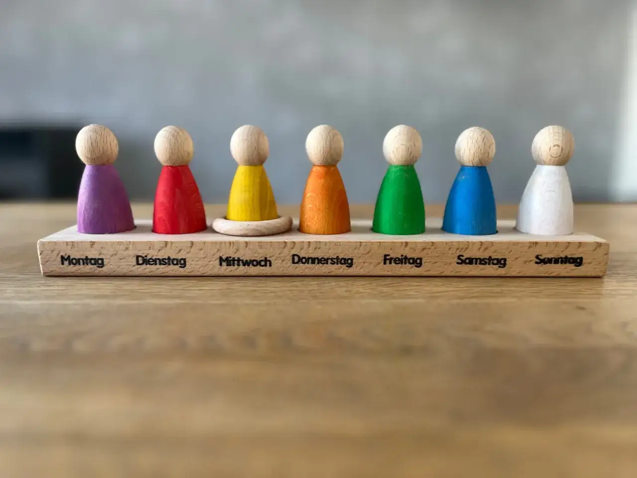 Holzfiguren in Regenbogenfarben helfen beim wochentage lernen montessori. Jeder Tag hat eine eigene Farbe und Beschriftung.