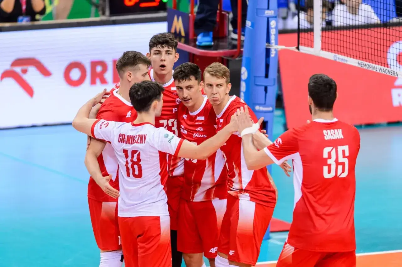 Siatkarze reprezentacji Polski w czerwonych strojach świętują zwycięstwo. Rozgrywający z numerem 18, Graniezny, jest w centrum uwagi.
