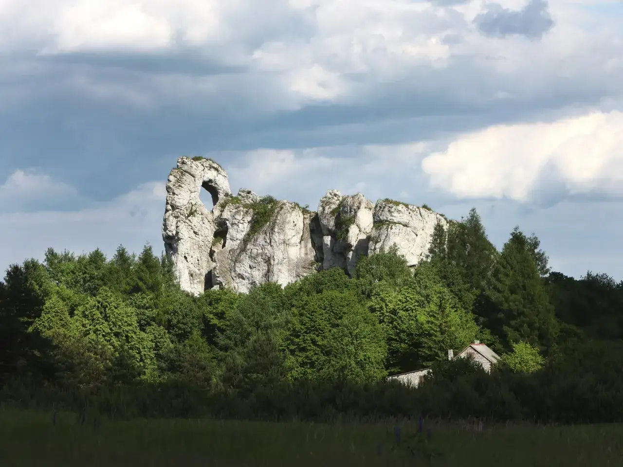 Imponujący okiennik wielki, skalna brama wśród zieleni, z ukrytą chatką.