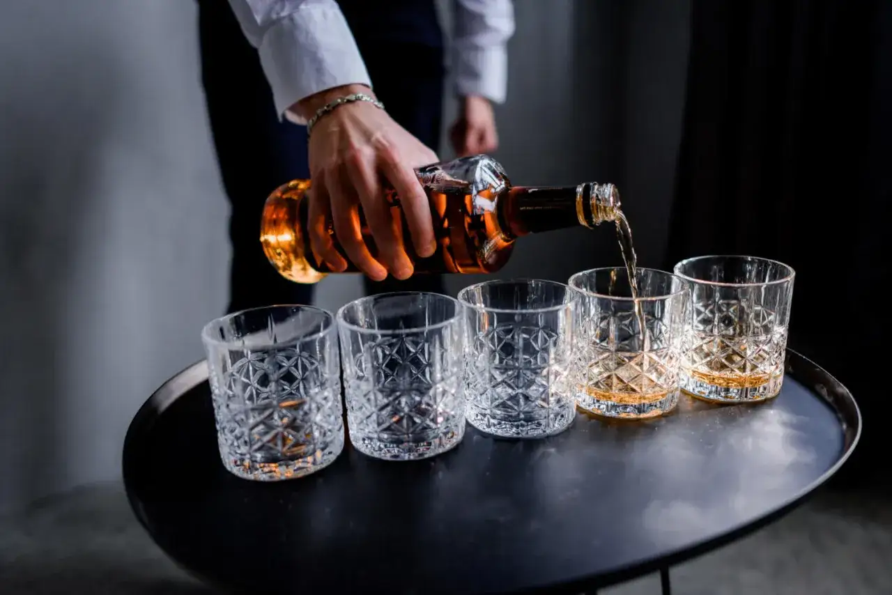 Elegancki mężczyzna nalewa whisky do kieliszk&oacute;w. Idealny dzień whisky, by uczcić wyjątkowe chwile.