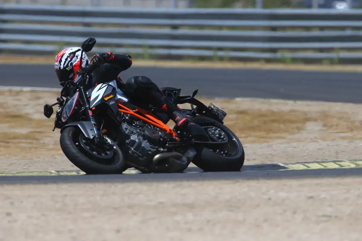 Motociclista con casco y visera oscura, inclinado en una curva. La moto, con detalles naranjas, luce una multa por exceso de velocidad.