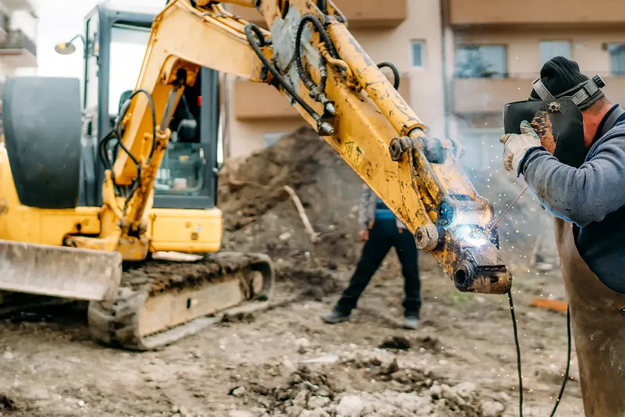 Spawacz naprawia koparkę, która pomoże zdecydować, czym zasypać fundamenty.