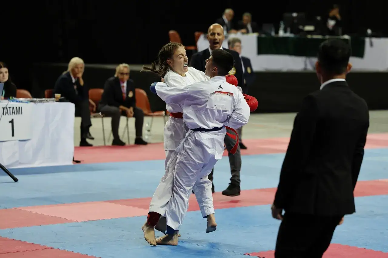 Dwoje zawodników w białych kimonach walczy na macie. To właśnie jest sparing, dynamiczna walka treningowa, która przygotowuje do zawodów.