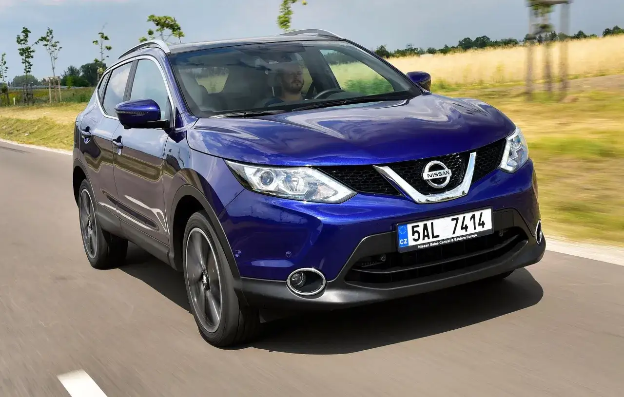 Niebieski Nissan Qashqai 2 jedzie po drodze, za kierownicą siedzi mężczyzna.