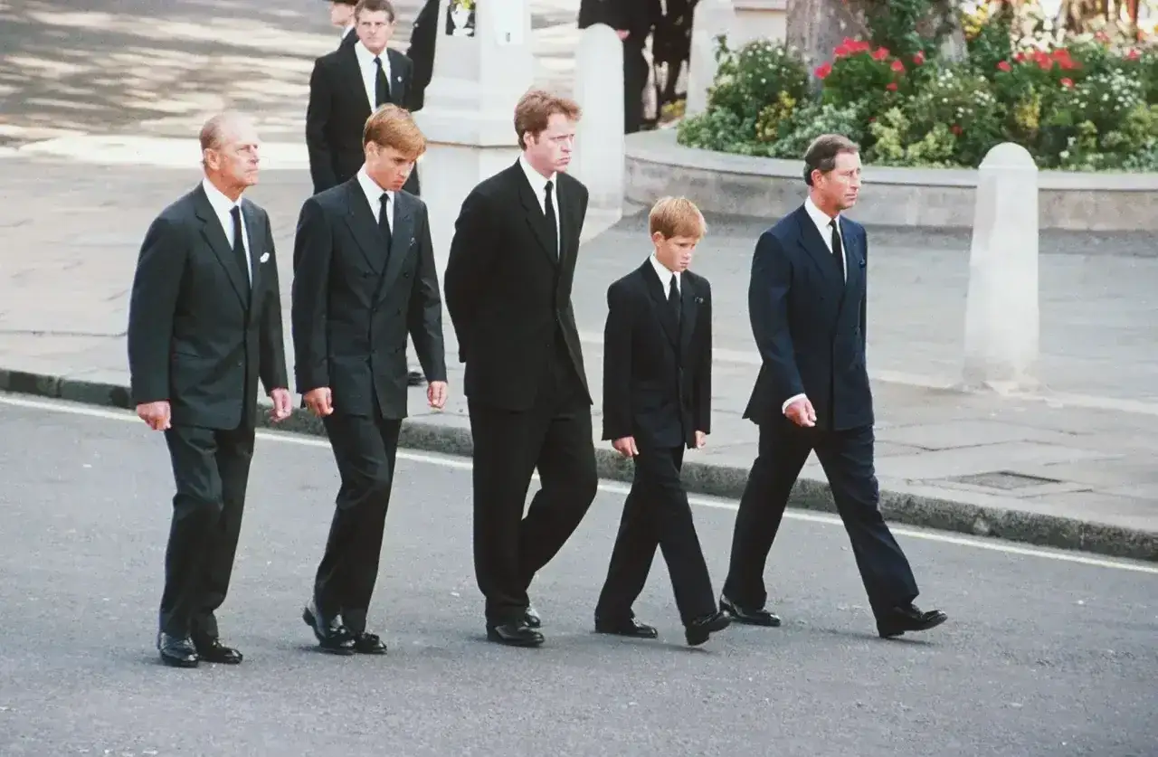 Kr&oacute;lewscy mężczyźni w czarnych garniturach i białych koszulach na pogrzebie. Książę Filip, książę William, książę Harry i książę Karol idą obok siebie.