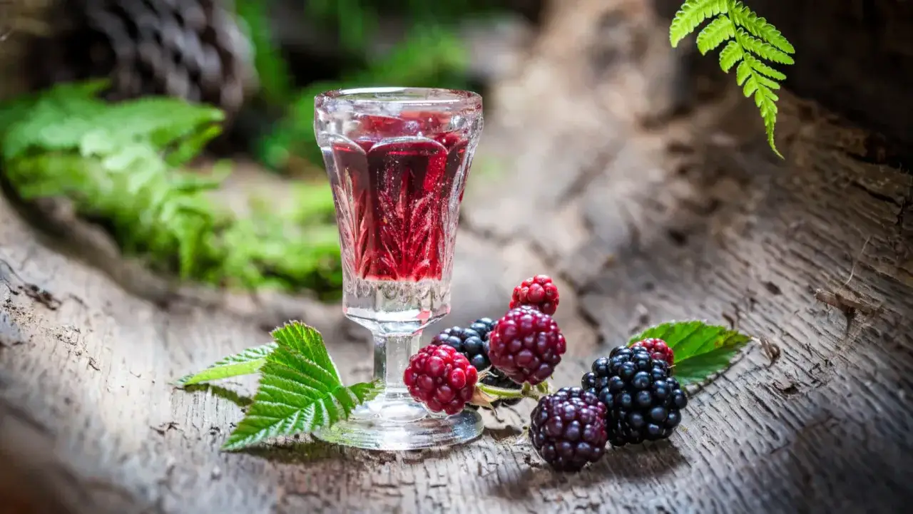 Ein Glas roter Likör neben frischen Brombeeren und Himbeeren. Ein ideales Rezept für schnaps selber machen rezept.