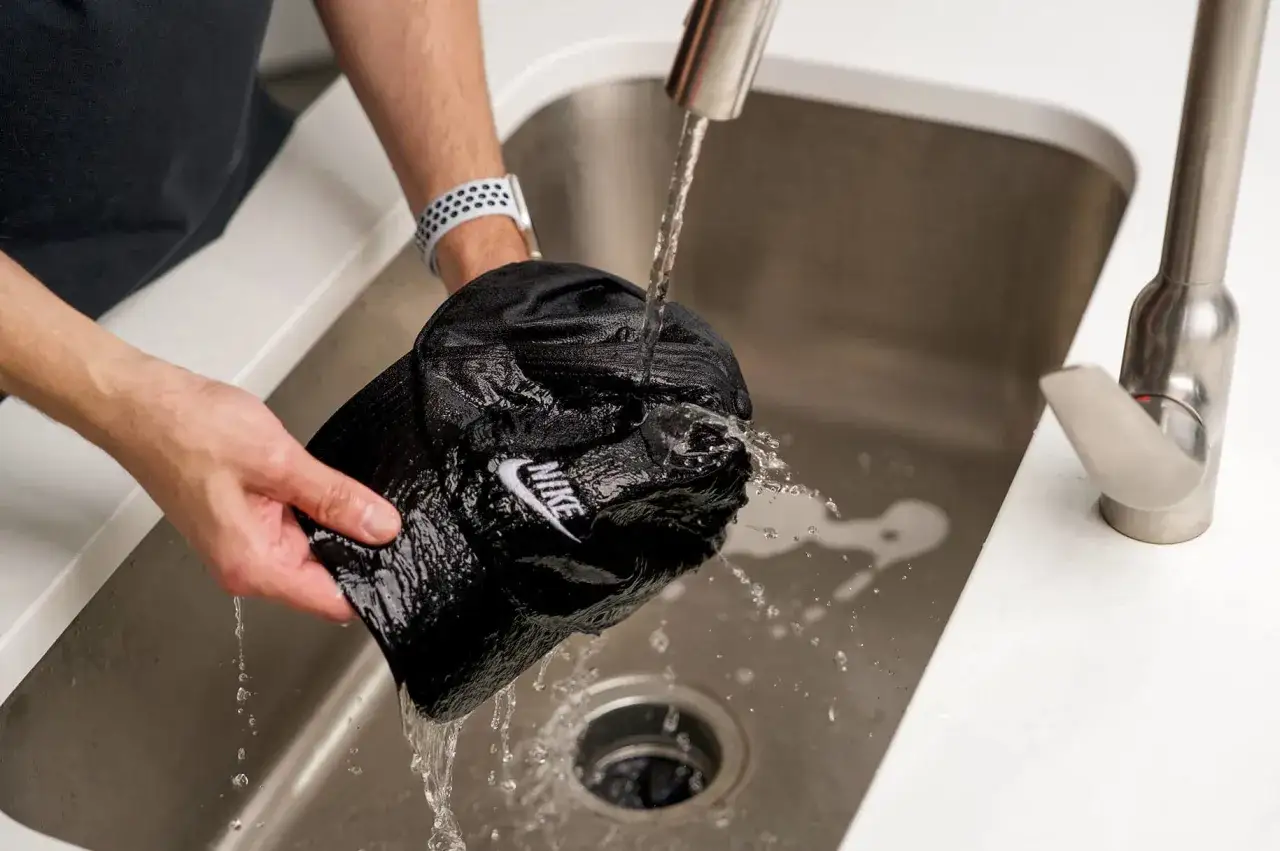 H&auml;nde waschen die schwarze Nike-Kappe unter flie&szlig;endem Wasser in der Sp&uuml;le.