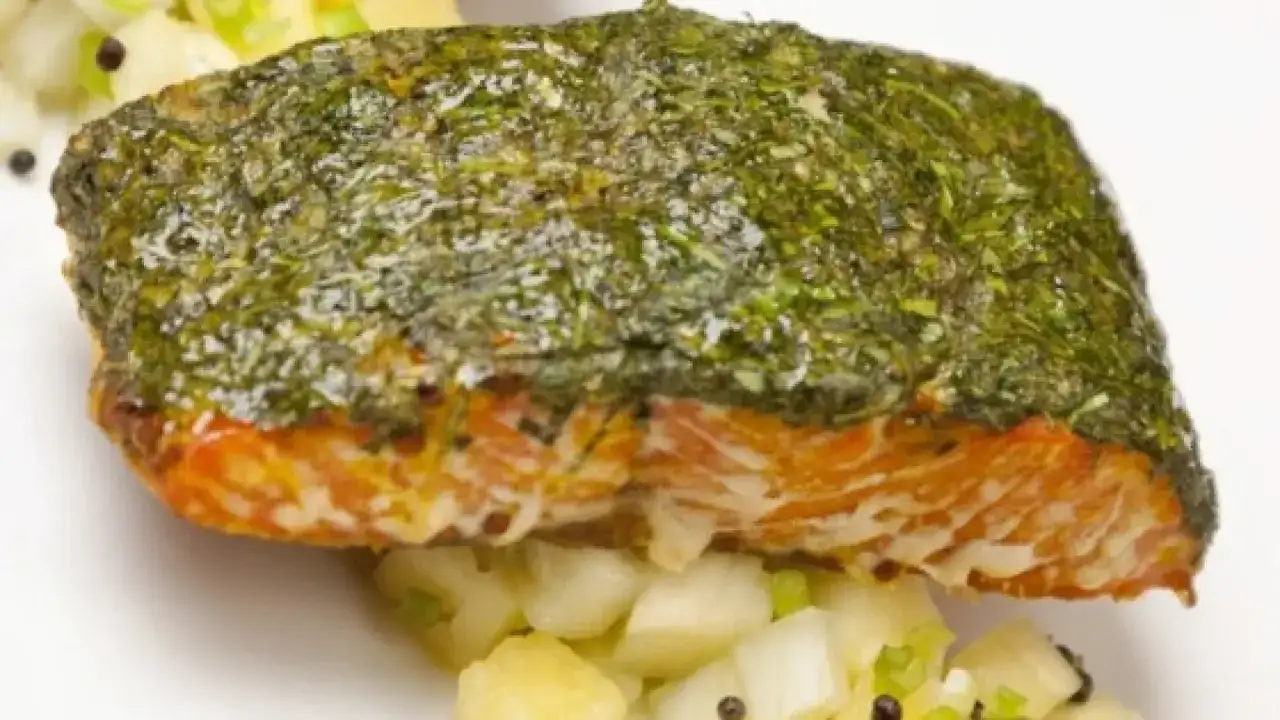 Delicioso pescado al horno cubierto de hierbas frescas, servido sobre una cama de patatas y cebolleta.