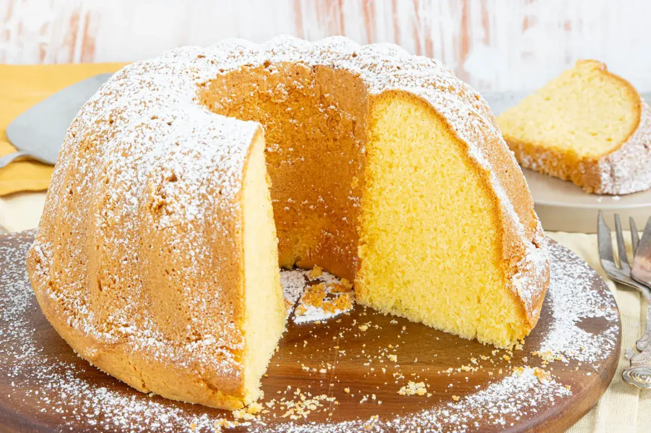 Ein saftiger vanille kuchen, mit Puderzucker best&auml;ubt, wird auf einem Holzbrett pr&auml;sentiert. Ein St&uuml;ck ist bereits angeschnitten.