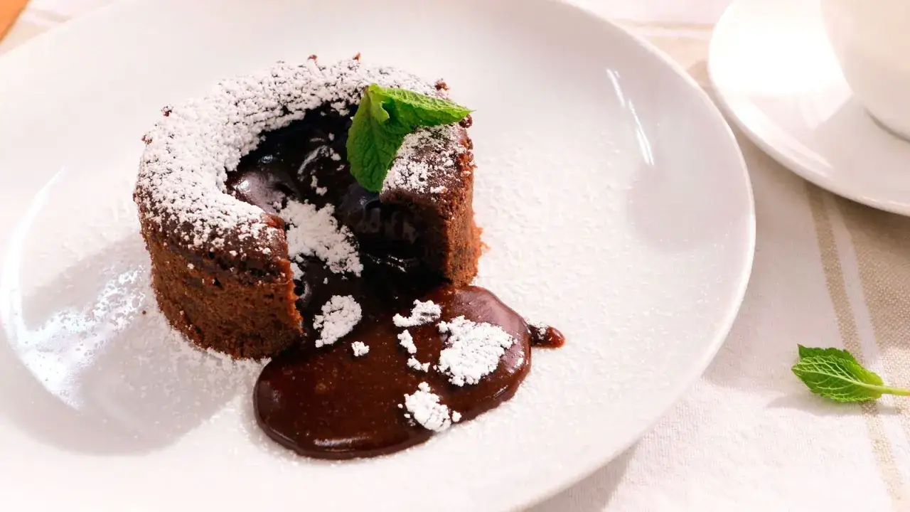 Coulant de chocolate con interior fundido, espolvoreado con azúcar glas y decorado con una hoja de menta.