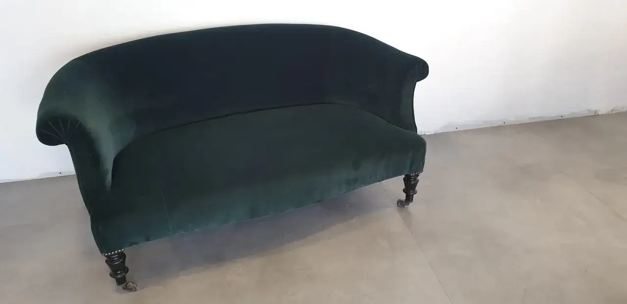 Banquette Napoléon III en velours vert profond, avec pieds sculptés et roulettes. Un meuble élégant pour un salon d'époque.