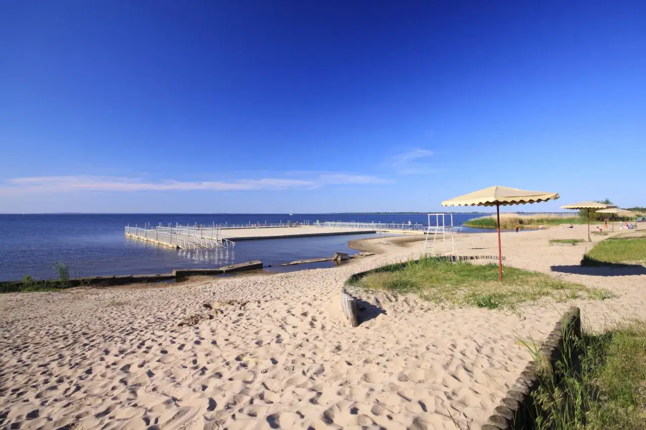 Plaża z pomostem i parasolami. W tle błękitne niebo i spokojna woda. Idealne miejsce na wypoczynek, zastanawiasz się, ile jest ze Szczecina do morza?