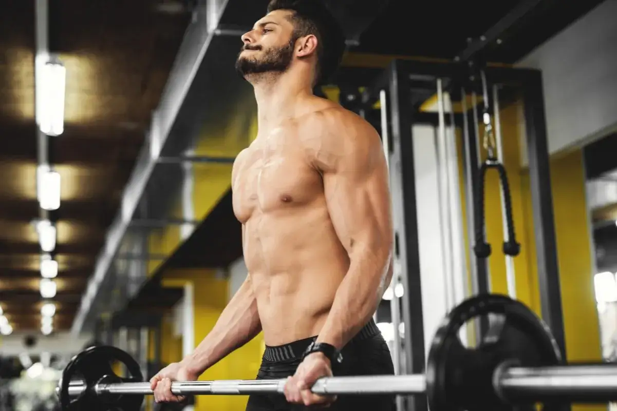 Mężczyzna z wyrzeźbionym brzuchem podnosi sztangę. Czy trening siłowy spala tłuszcz? Tak, budowanie mięśni przyspiesza metabolizm.