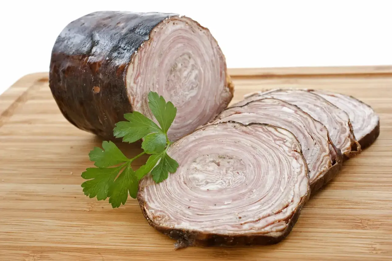 Andouillette tranchée sur planche en bois, avec persil. Une image pour comprendre la différence entre andouille et andouillette.