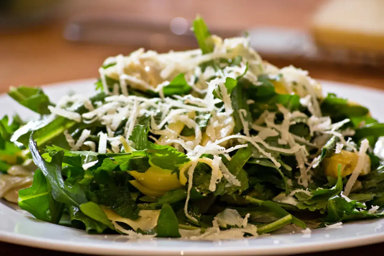Frischer, grüner **artischocken salat** mit geriebenem Käse bestreut, serviert auf einem weißen Teller.
