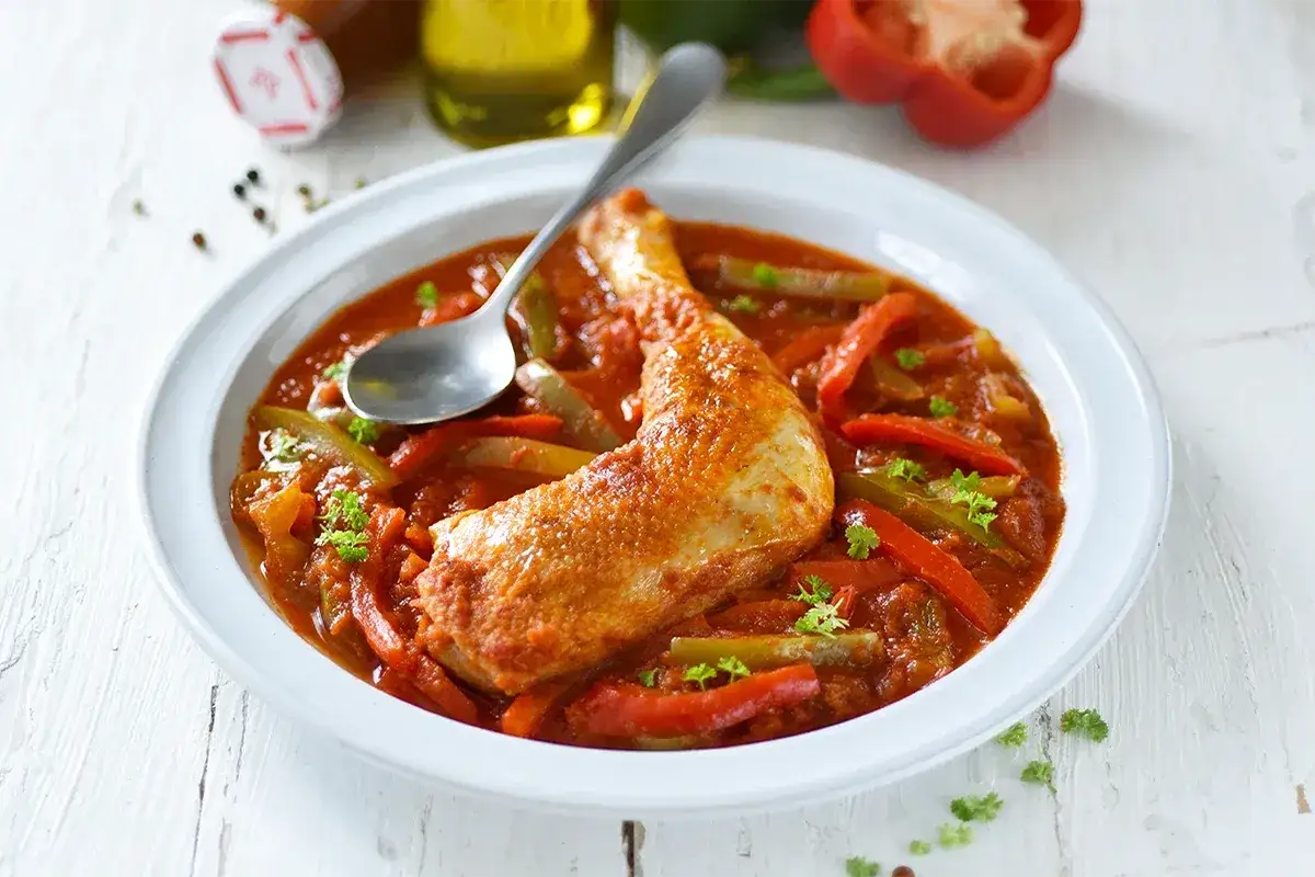 Un plat de poulet basquaise de ma grand-mère, avec des poivrons rouges et verts dans une sauce tomate savoureuse.