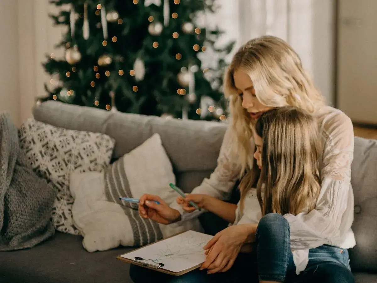 Madre e hija dibujan juntas, creando su propio cuento de navidad corto, con un &aacute;rbol decorado de fondo.