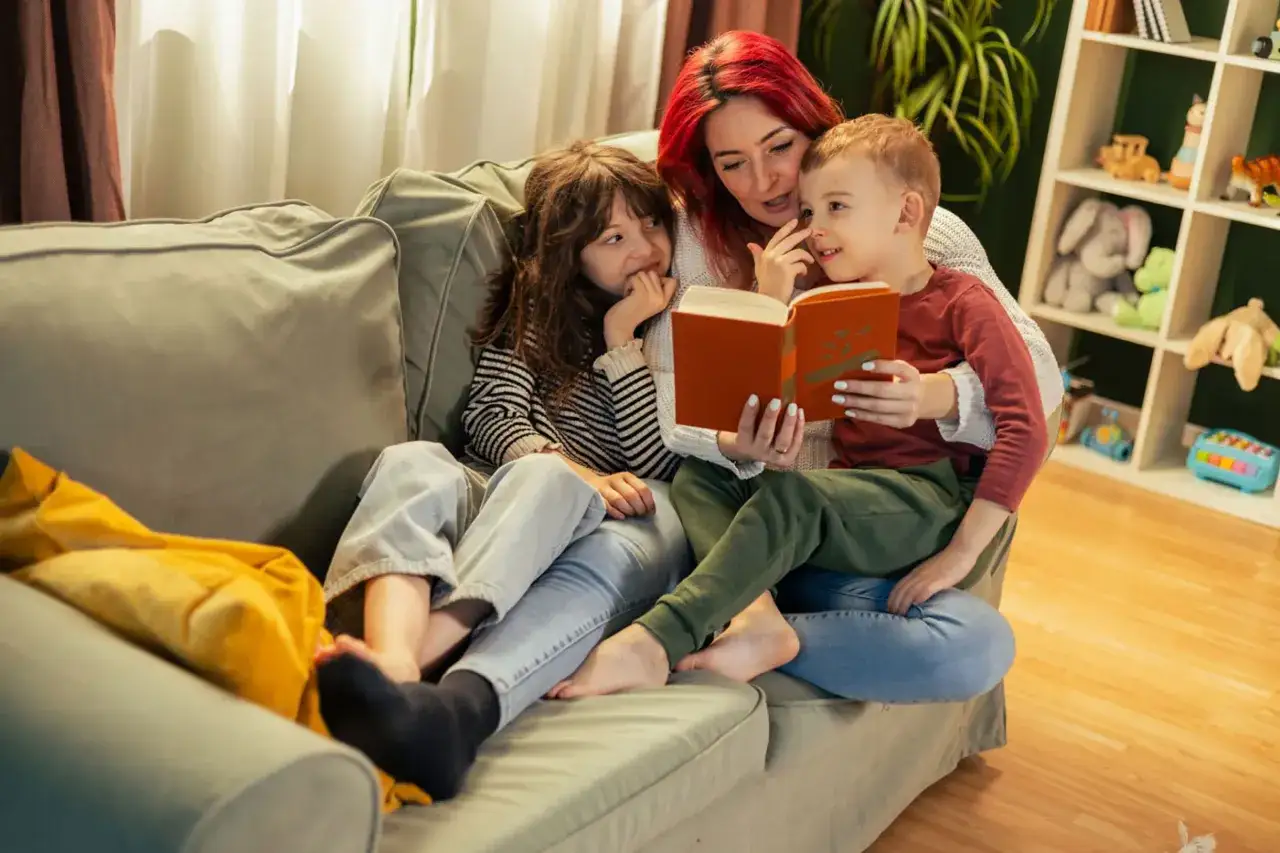 Mutter liest Kindern auf dem Sofa vor. Ein Junge, vielleicht 3 Jahre alt, lauscht gespannt. F&ouml;rderung der Sprachentwicklung 3 Jahre durch gemeinsames Lesen.