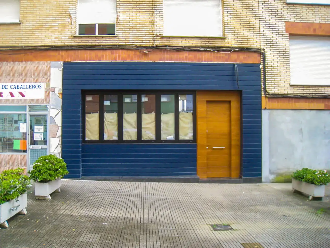 Fachadas de locales convertidos en viviendas, con un local azul moderno y una puerta de madera, junto a un edificio de ladrillo.