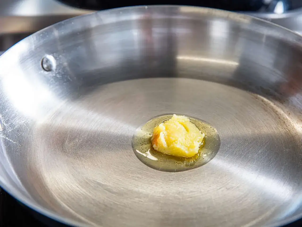 Ein Klumpen Ghee schmilzt in einer Pfanne. Ghee ist geklärte Butter, die beim Kochen für ein nussiges Aroma sorgt.