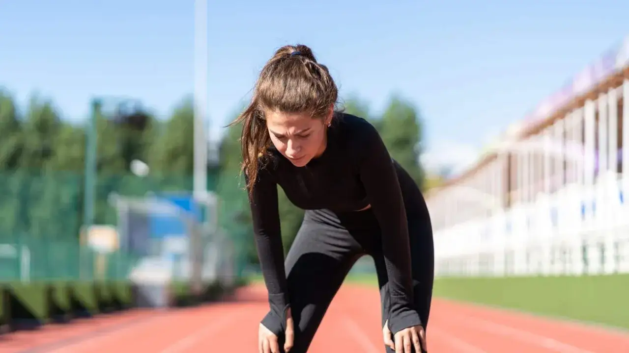 Atleta esausta sulla pista, cerca rimedi per l'overtraining.