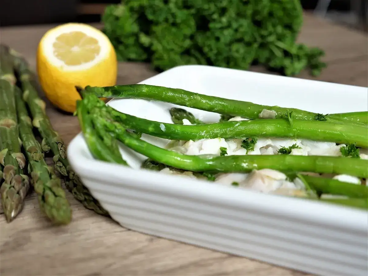 Asperges vertes sur un lit de poisson blanc, garnies de persil frais et napp&eacute;es d'une d&eacute;licieuse sauce beurre blanc. Un citron jaune &agrave; c&ocirc;t&eacute;.