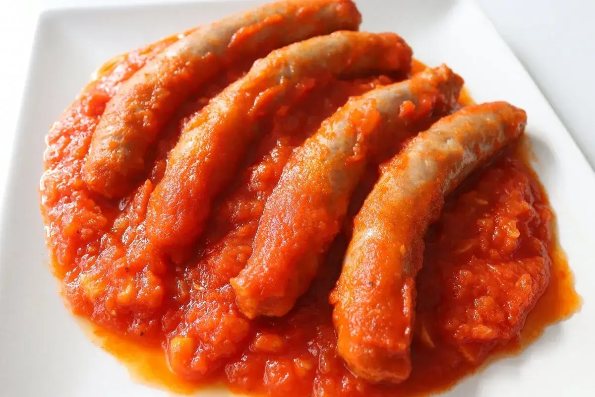 Cuatro salchichas bañadas en una salsa de tomate casera, servidas en un plato blanco.