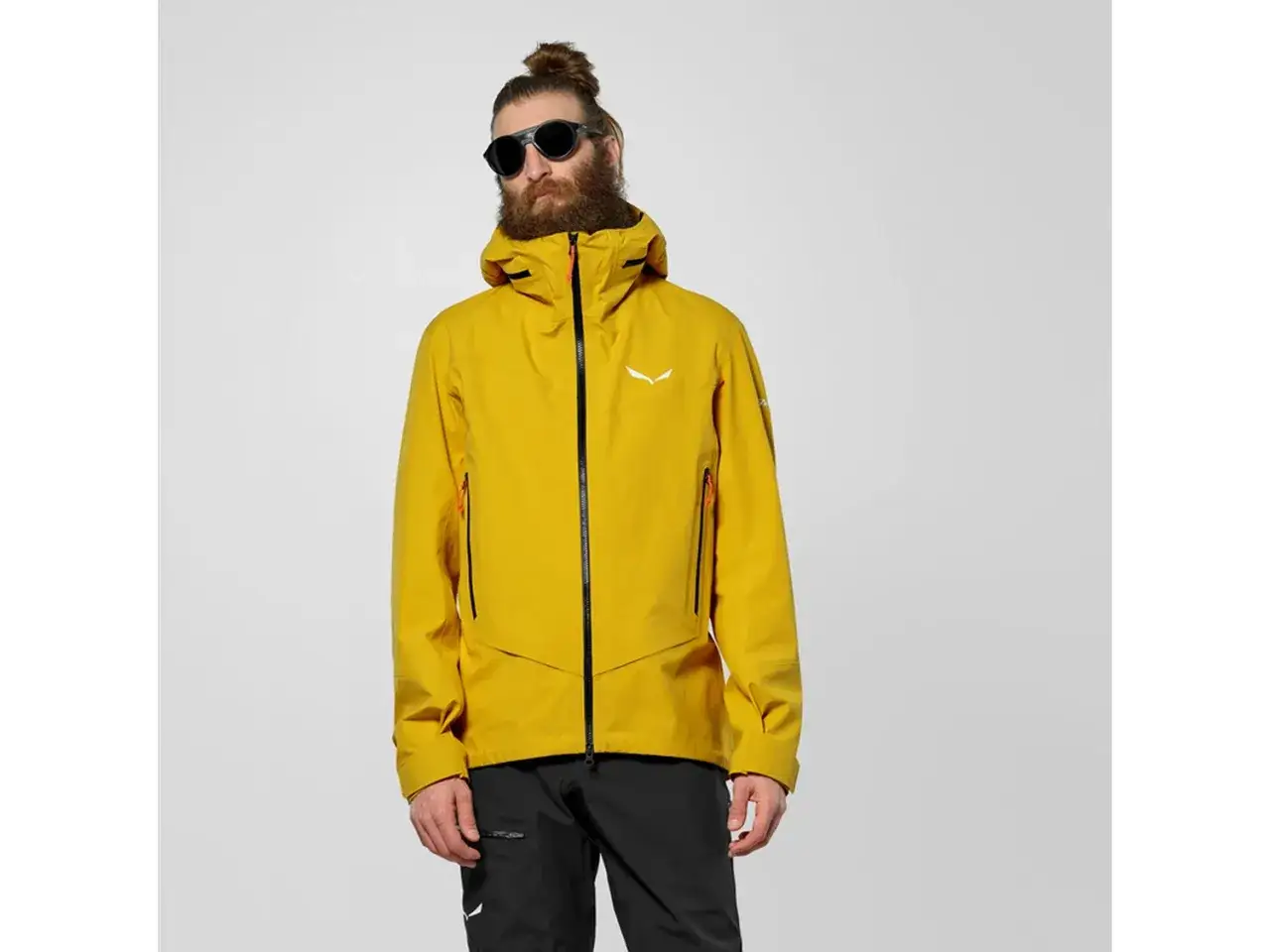 Mężczyzna w ż&oacute;łtej kurtce z kapturem i czarnymi spodniami. Kurtka posiada membranę Gore-Tex, chroniącą przed deszczem i wiatrem.