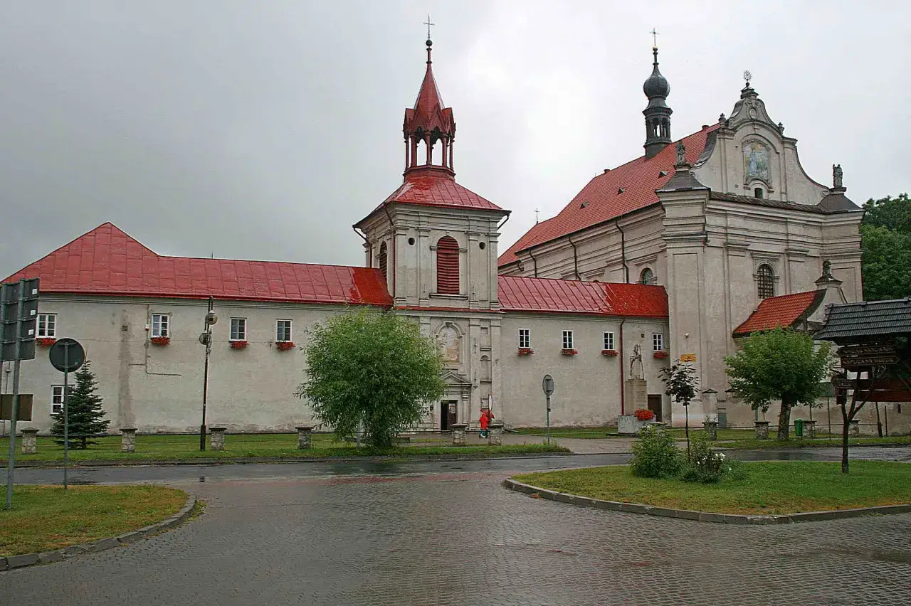 Krasnobród atrakcje: zabytkowy zespół klasztorny z czerwonymi dachami i wieżą, otoczony zielenią i brukowanym placem.