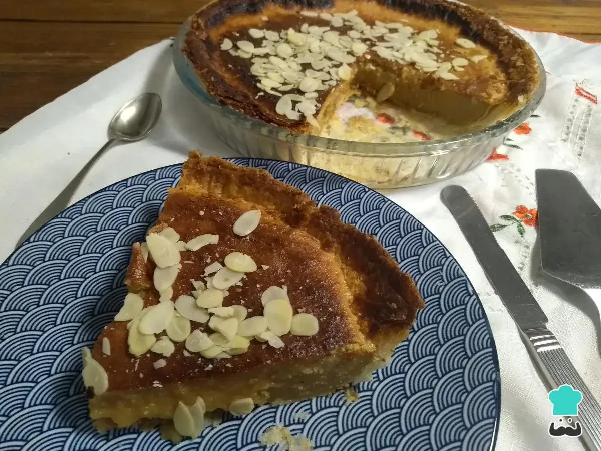 Un trozo de bizcocho de almendra de la abuela, espolvoreado con láminas de almendra, servido en un plato azul y blanco.