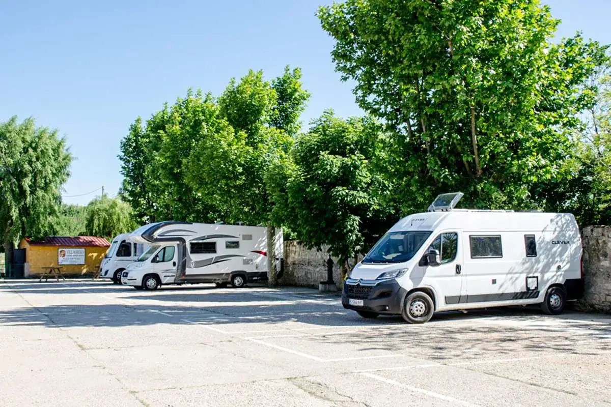 Un garaje para caravanas con varios vehículos aparcados bajo árboles frondosos.