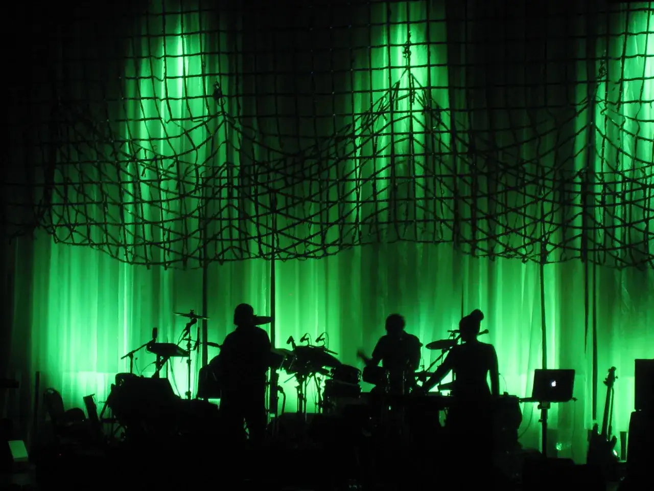 Silhouettes muzyków na scenie podczas koncertu Dead Can Dance, w zielonym, hipnotyzującym świetle.