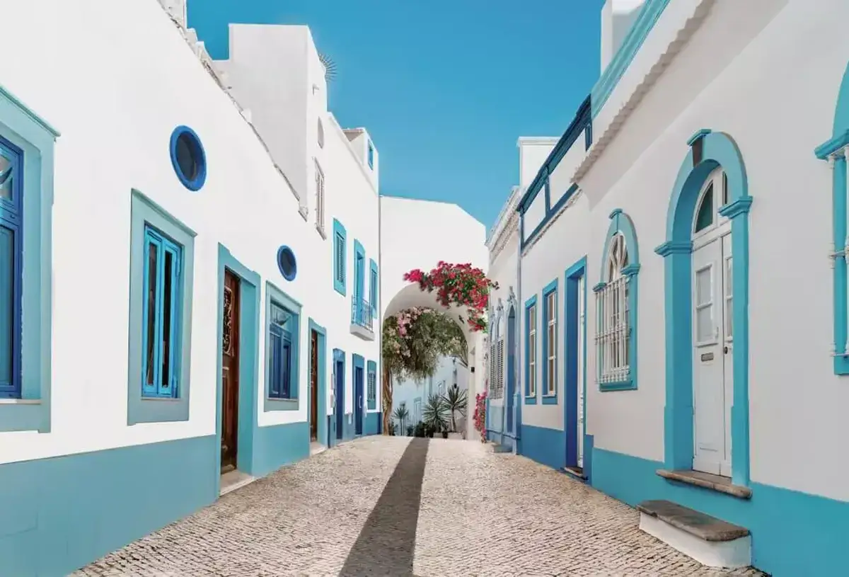 Eine sonnige Gasse im Distrikt Faro, Portugal, mit wei&szlig; get&uuml;nchten H&auml;usern und leuchtend blauen Akzenten.