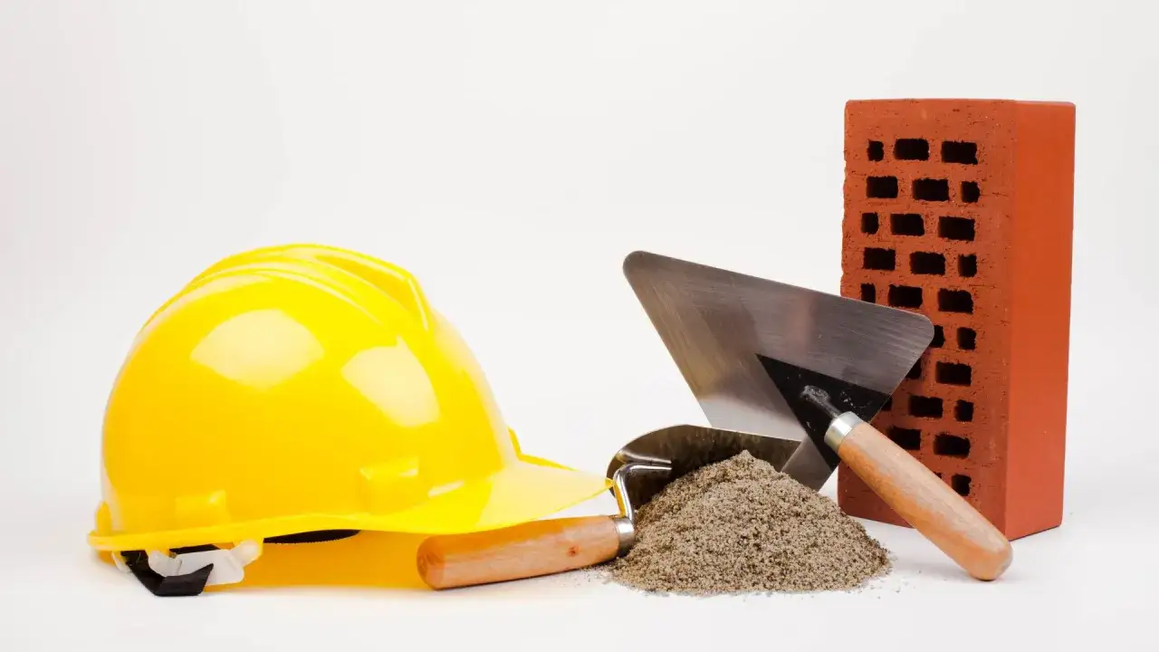 Casque jaune, brique rouge, tas de sable et truelles : les outils maçon essentiels pour bâtir.