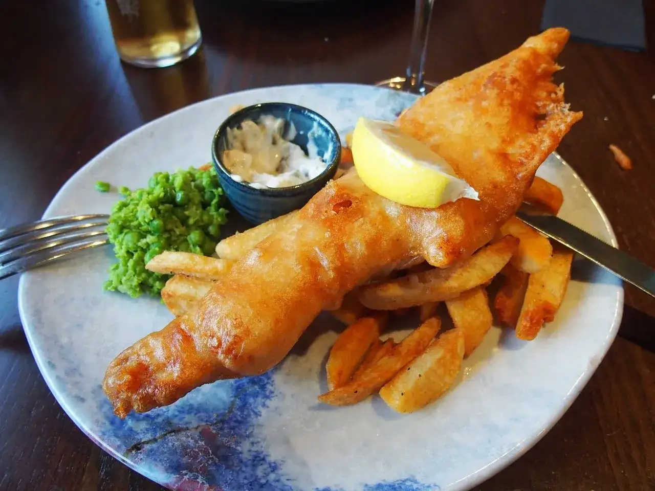 Un delicioso plato t&iacute;pico ingl&eacute;s: pescado rebozado crujiente, patatas fritas doradas, guisantes tiernos y una salsa cremosa.